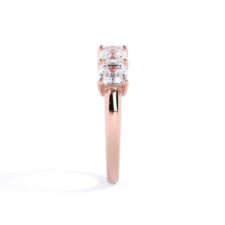 A picture of a five stone diamond wedding ring with asscher shape diamonds that are shared prong set in rose gold on a white background with a side profile view.