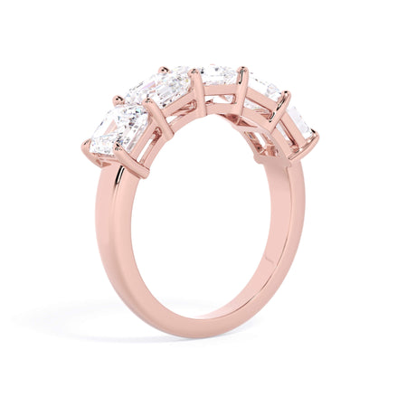 A picture of a five stone diamond wedding ring with asscher shape diamonds that are shared prong set in rose gold on a white background with a slightly angled, through the finger view.