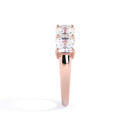 A picture of a five stone diamond wedding ring with asscher shape diamonds that are shared prong set in rose gold on a white background with a side profile view.