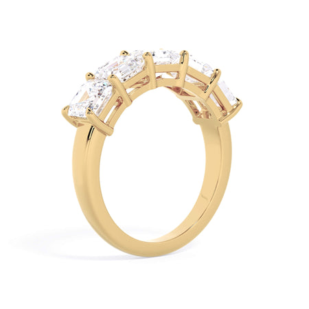 A picture of a five stone diamond wedding ring with asscher shape diamonds that are shared prong set in yellow gold on a white background with a slightly angled, through the finger view.