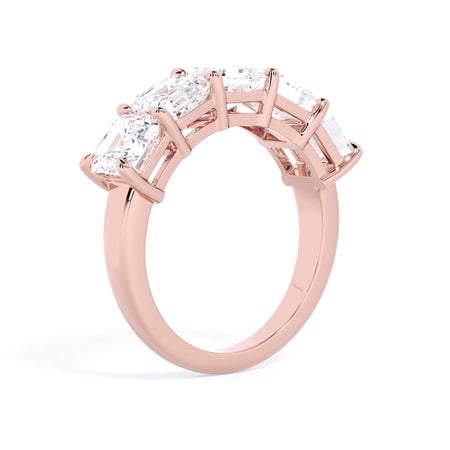 A picture of a five stone diamond wedding ring with asscher shape diamonds that are shared prong set in rose gold on a white background with a slightly angled, through the finger view.