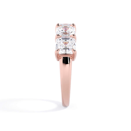 A picture of a five stone diamond wedding ring with asscher shape diamonds that are shared prong set in rose gold on a white background with a side profile view.
