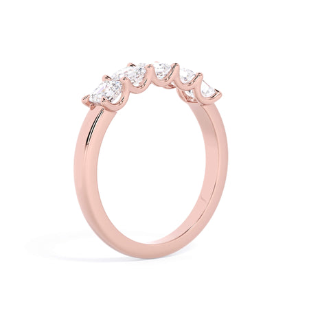 A picture of a five stone diamond wedding ring with asscher shape diamonds that are u prong set in rose gold on a white background with a slightly angled, through the finger view.
