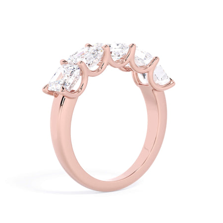 A picture of a five stone diamond wedding ring with asscher shape diamonds that are u prong set in rose gold on a white background with a slightly angled, through the finger view.