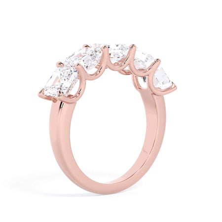 A picture of a five stone diamond wedding ring with asscher shape diamonds that are u prong set in rose gold on a white background with a slightly angled, through the finger view.