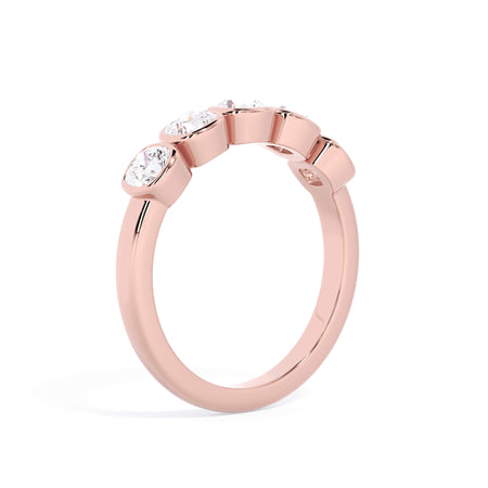 A picture of a five stone diamond wedding ring with cushion shape diamonds that are bezel set in rose gold on a white background with a slightly angled, through the finger view.