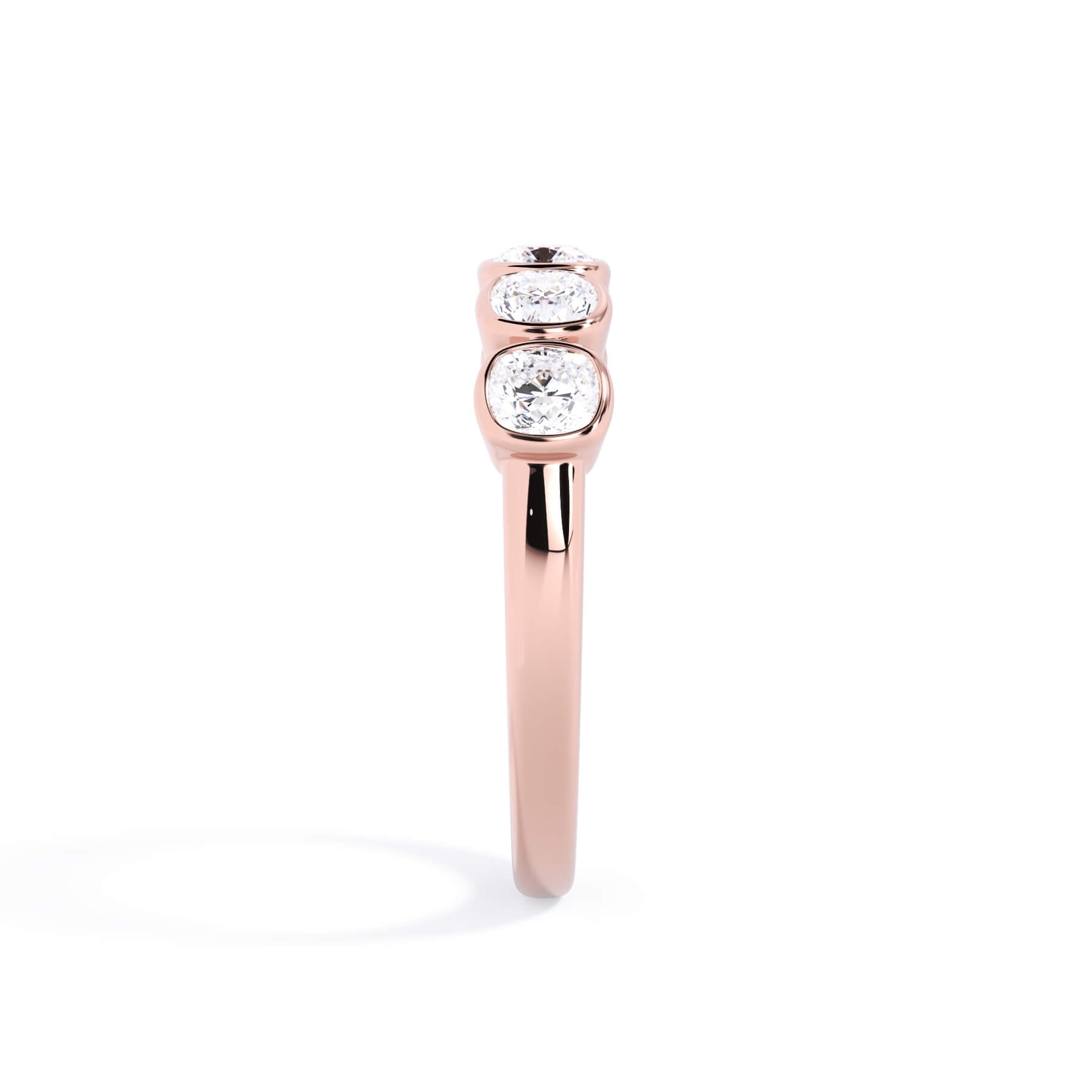 A picture of a five stone diamond wedding ring with cushion shape diamonds that are bezel set in rose gold on a white background with a side profile view.