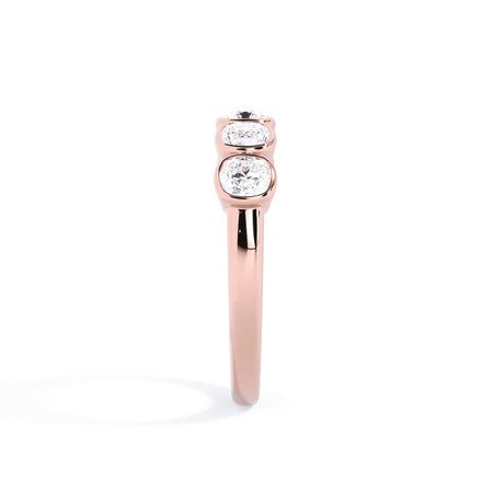 A picture of a five stone diamond wedding ring with cushion shape diamonds that are bezel set in rose gold on a white background with a side profile view.