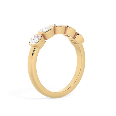 A picture of a five stone diamond wedding ring with cushion shape diamonds that are bezel set in yellow gold on a white background with a slightly angled, through the finger view.