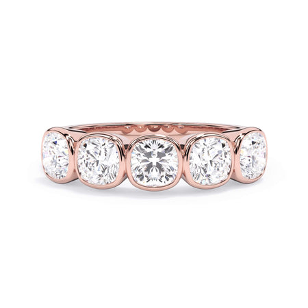 A picture of a five stone diamond wedding ring with cushion shape diamonds that are bezel set in rose gold on a white background with the ring facing forward, lying down.