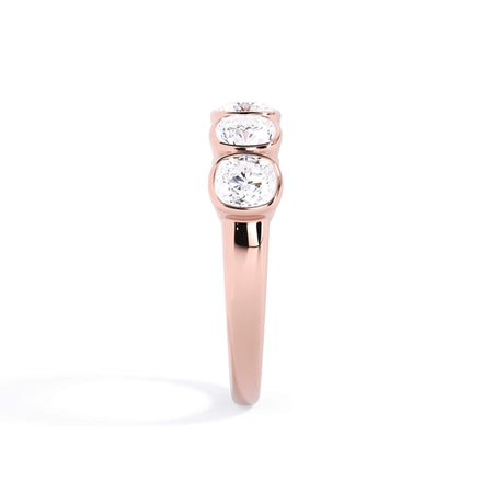 A picture of a five stone diamond wedding ring with cushion shape diamonds that are bezel set in rose gold on a white background with a side profile view.