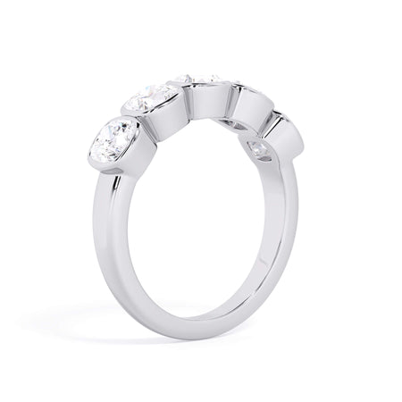 A picture of a five stone diamond wedding ring with cushion shape diamonds that are bezel set in white gold or platinum on a white background with a slightly angled, through the finger view.
