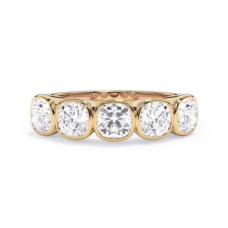 A picture of a five stone diamond wedding ring with cushion shape diamonds that are bezel set in yellow gold on a white background with the ring facing forward, lying down.