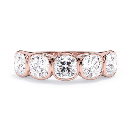 A picture of a five stone diamond wedding ring with cushion shape diamonds that are bezel set in rose gold on a white background with the ring facing forward, lying down.