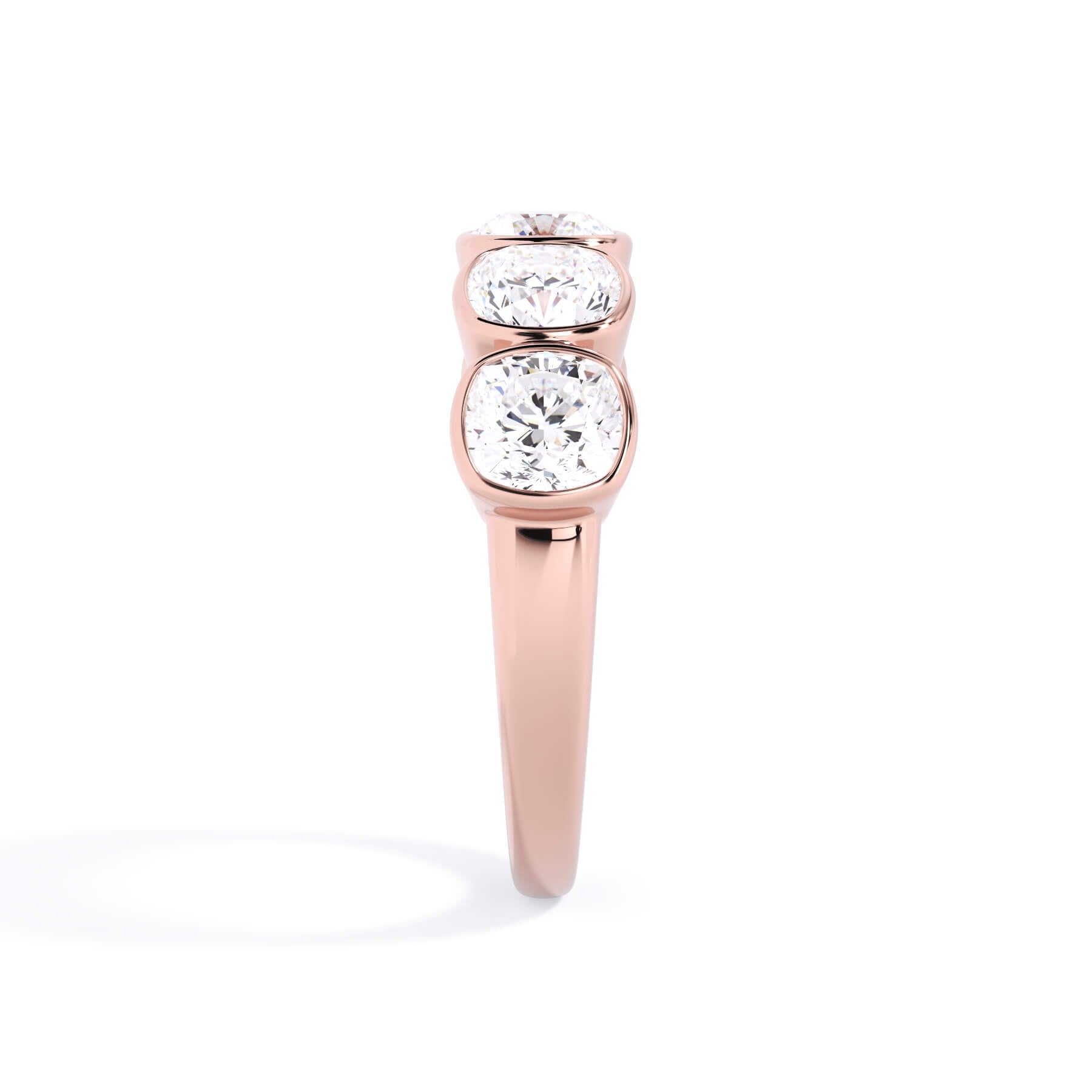 A picture of a five stone diamond wedding ring with cushion shape diamonds that are bezel set in rose gold on a white background with a side profile view.