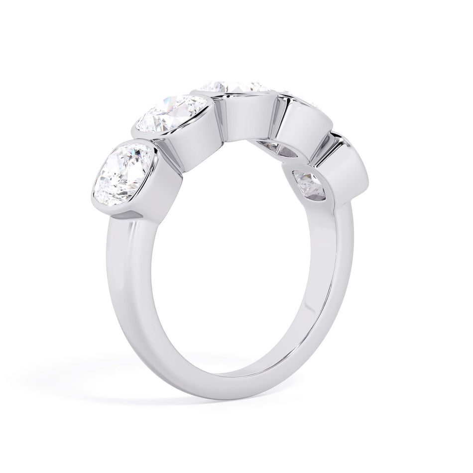 A picture of a five stone diamond wedding ring with cushion shape diamonds that are bezel set in white gold or platinum on a white background with a slightly angled, through the finger view.
