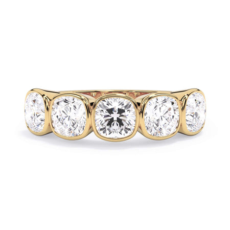 A picture of a five stone diamond wedding ring with cushion shape diamonds that are bezel set in yellow gold on a white background with the ring facing forward, lying down.