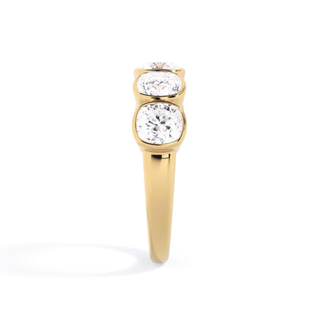 A picture of a five stone diamond wedding ring with cushion shape diamonds that are bezel set in yellow gold on a white background with a side profile view.