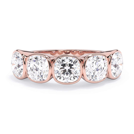 A picture of a five stone diamond wedding ring with cushion shape diamonds that are bezel set in rose gold on a white background with the ring facing forward, lying down.