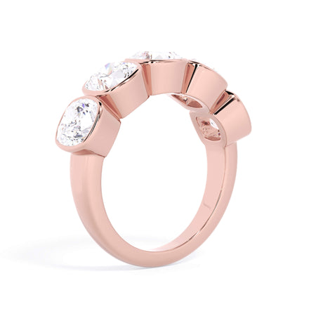 A picture of a five stone diamond wedding ring with cushion shape diamonds that are bezel set in rose gold on a white background with a slightly angled, through the finger view.