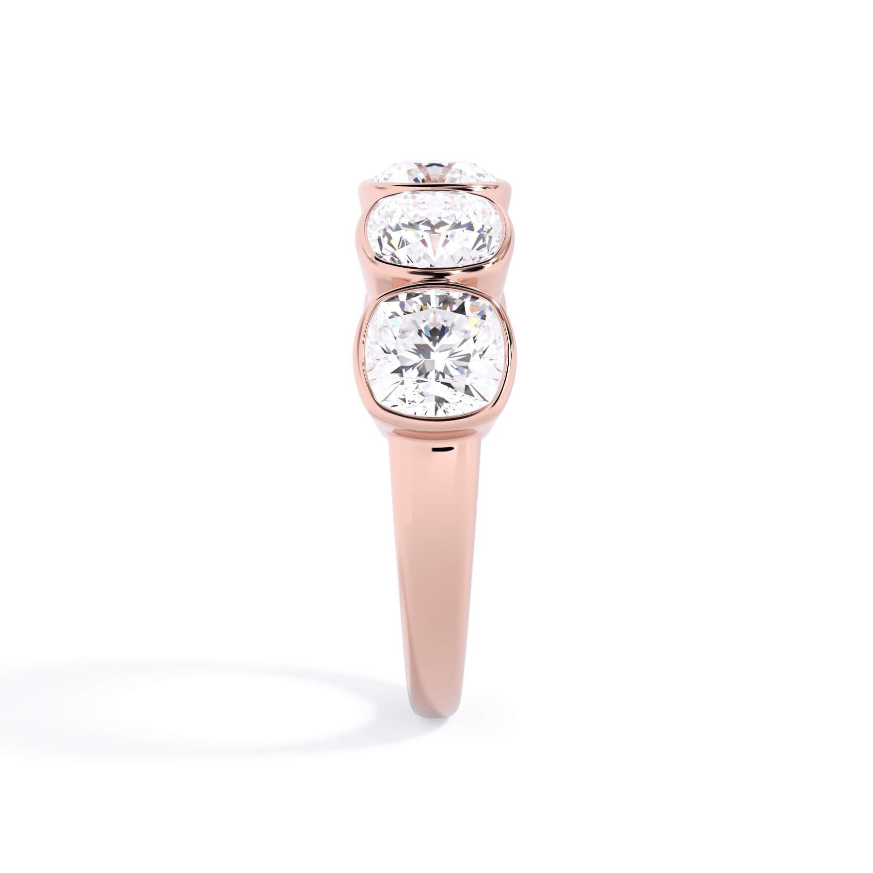 A picture of a five stone diamond wedding ring with cushion shape diamonds that are bezel set in rose gold on a white background with a side profile view.