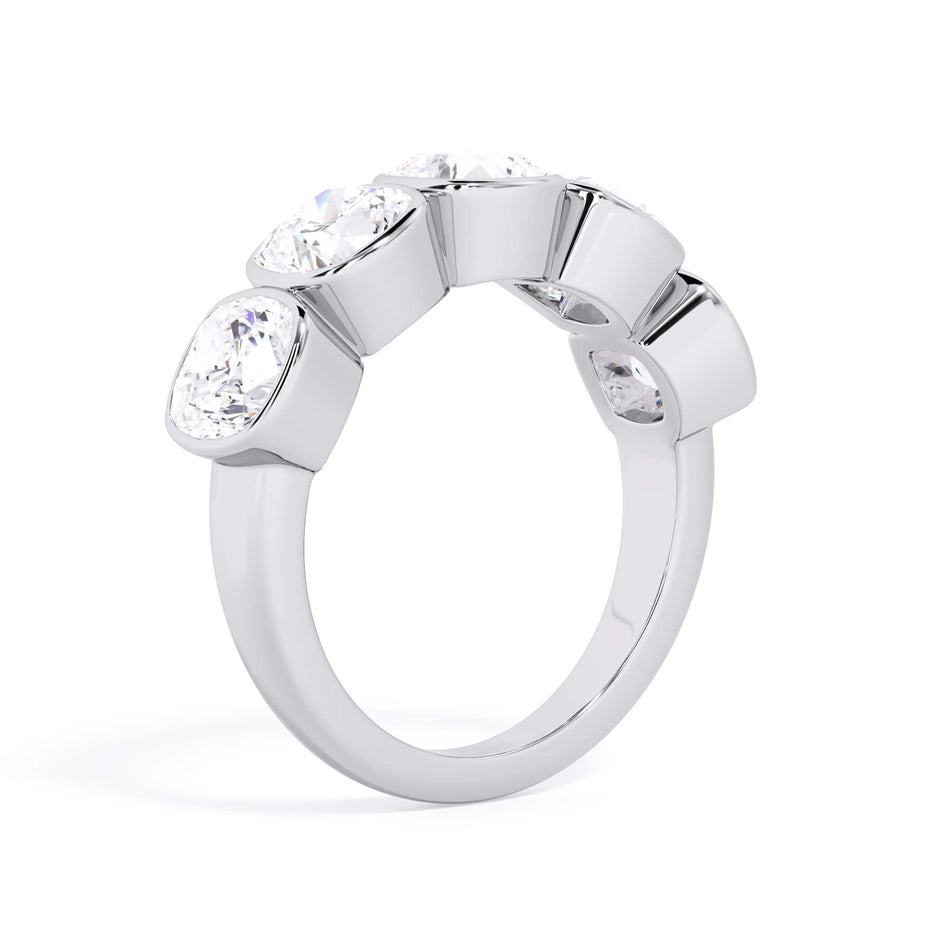 A picture of a five stone diamond wedding ring with cushion shape diamonds that are bezel set in white gold or platinum on a white background with a slightly angled, through the finger view.