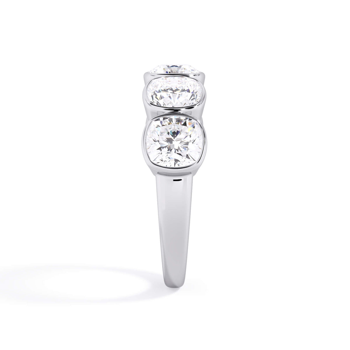 A picture of a five stone diamond wedding ring with cushion shape diamonds that are bezel set in white gold or platinum on a white background with a side profile view.