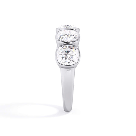 A picture of a five stone diamond wedding ring with cushion shape diamonds that are bezel set in white gold or platinum on a white background with a side profile view.