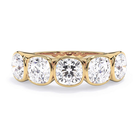 A picture of a five stone diamond wedding ring with cushion shape diamonds that are bezel set in yellow gold on a white background with the ring facing forward, lying down.