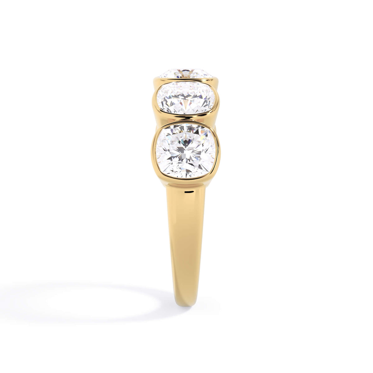 A picture of a five stone diamond wedding ring with cushion shape diamonds that are bezel set in yellow gold on a white background with a side profile view.