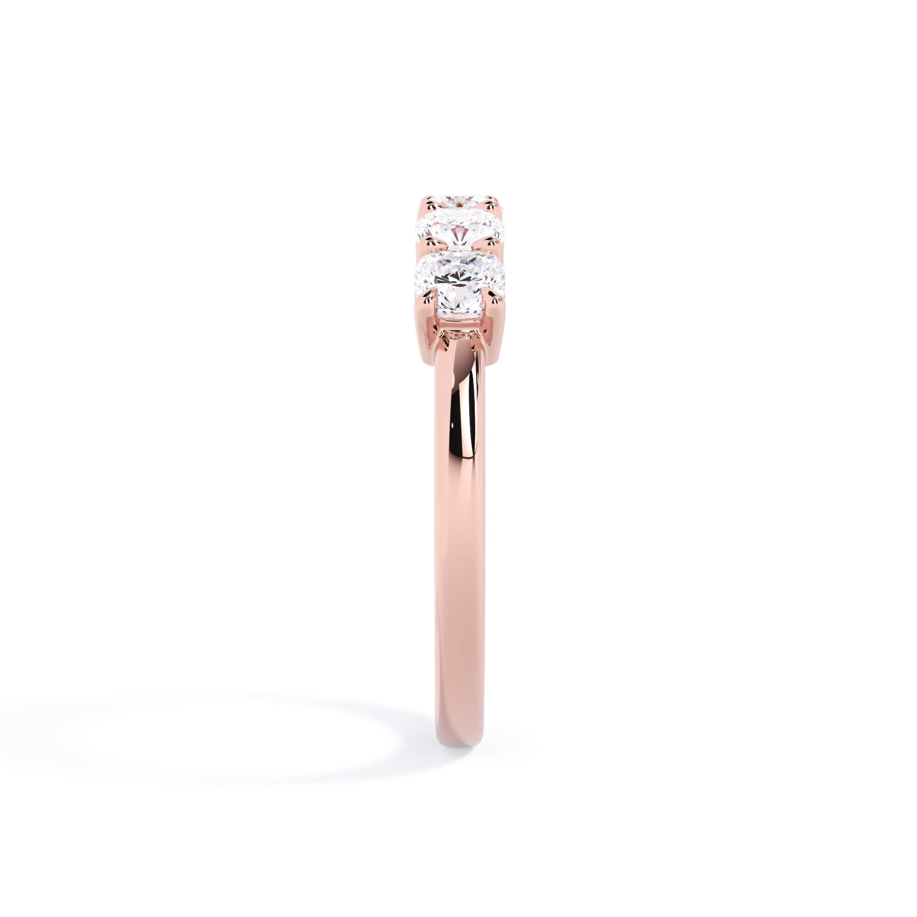 A picture of a five stone diamond wedding ring with cushion shape diamonds that are shared prong set in rose gold on a white background with a side profile view.