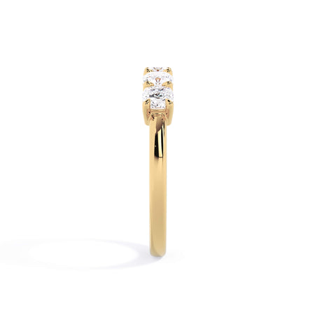 A picture of a five stone diamond wedding ring with cushion shape diamonds that are shared prong set in yellow gold on a white background with a side profile view.