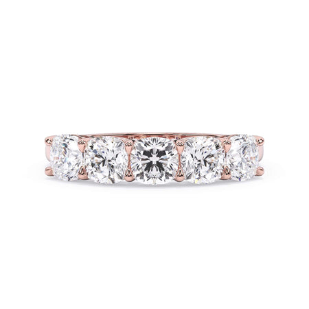 A picture of a five stone diamond wedding ring with cushion shape diamonds that are shared prong set in rose gold on a white background with the ring facing forward, lying down.