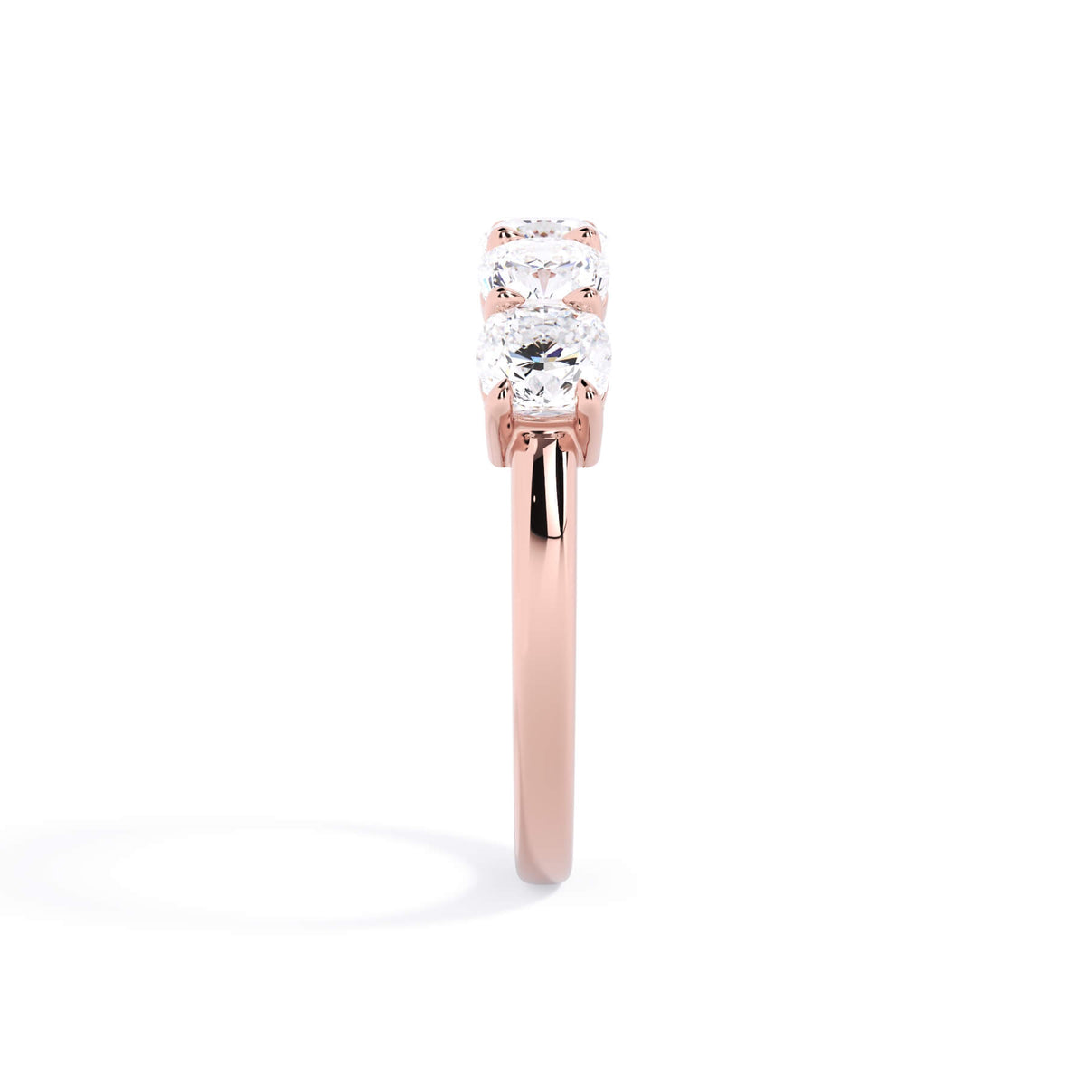 A picture of a five stone diamond wedding ring with cushion shape diamonds that are shared prong set in rose gold on a white background with a side profile view.