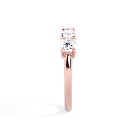A picture of a five stone diamond wedding ring with cushion shape diamonds that are shared prong set in rose gold on a white background with a side profile view.