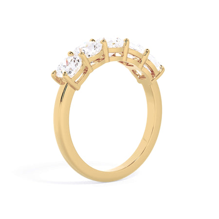 A picture of a five stone diamond wedding ring with cushion shape diamonds that are shared prong set in yellow gold on a white background with a slightly angled, through the finger view.