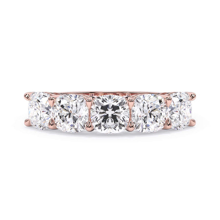 A picture of a five stone diamond wedding ring with cushion shape diamonds that are shared prong set in rose gold on a white background with the ring facing forward, lying down.