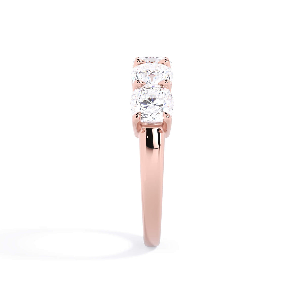 A picture of a five stone diamond wedding ring with cushion shape diamonds that are shared prong set in rose gold on a white background with a side profile view.