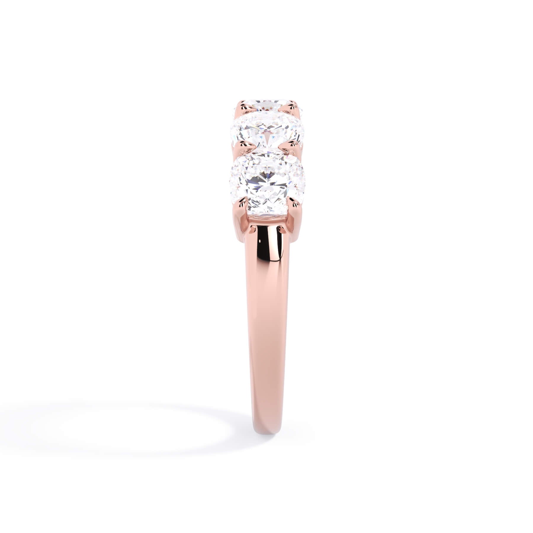 A picture of a five stone diamond wedding ring with cushion shape diamonds that are shared prong set in rose gold on a white background with a side profile view.