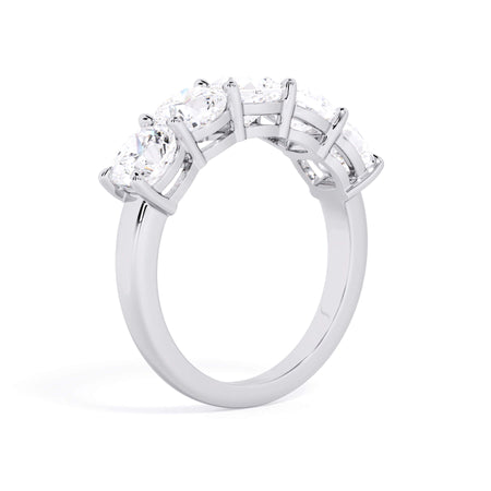 A picture of a five stone diamond wedding ring with cushion shape diamonds that are shared prong set in white gold or platinum on a white background with a slightly angled, through the finger view.