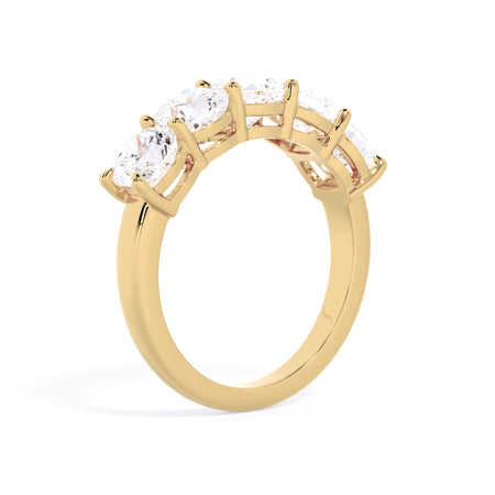 A picture of a five stone diamond wedding ring with cushion shape diamonds that are shared prong set in yellow gold on a white background with a slightly angled, through the finger view.