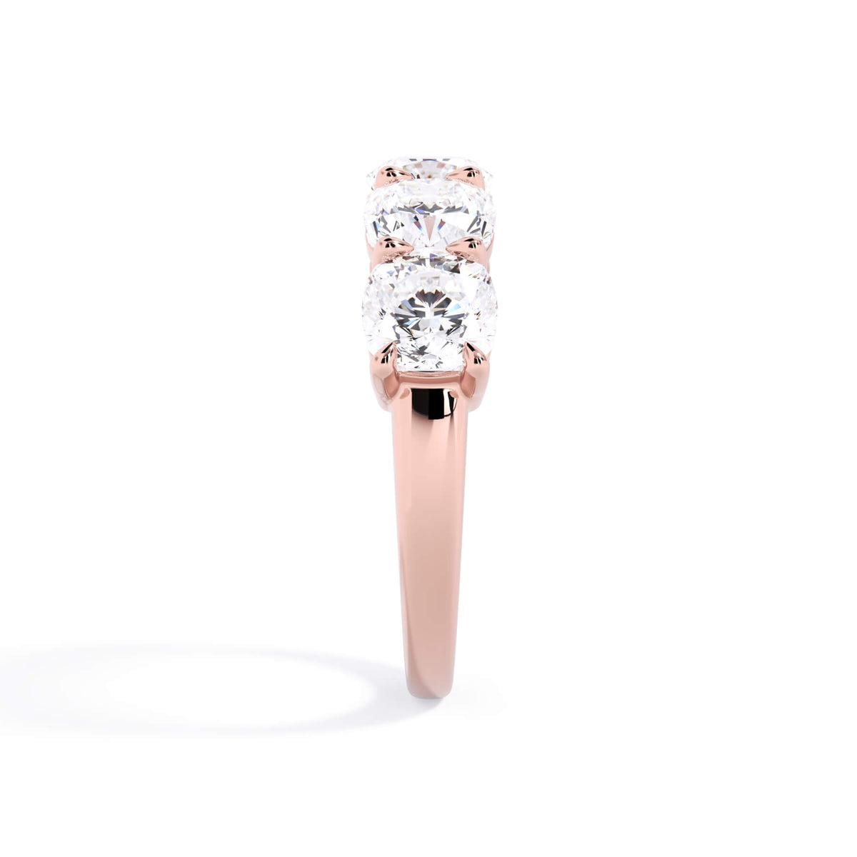 A picture of a five stone diamond wedding ring with cushion shape diamonds that are shared prong set in rose gold on a white background with a side profile view.