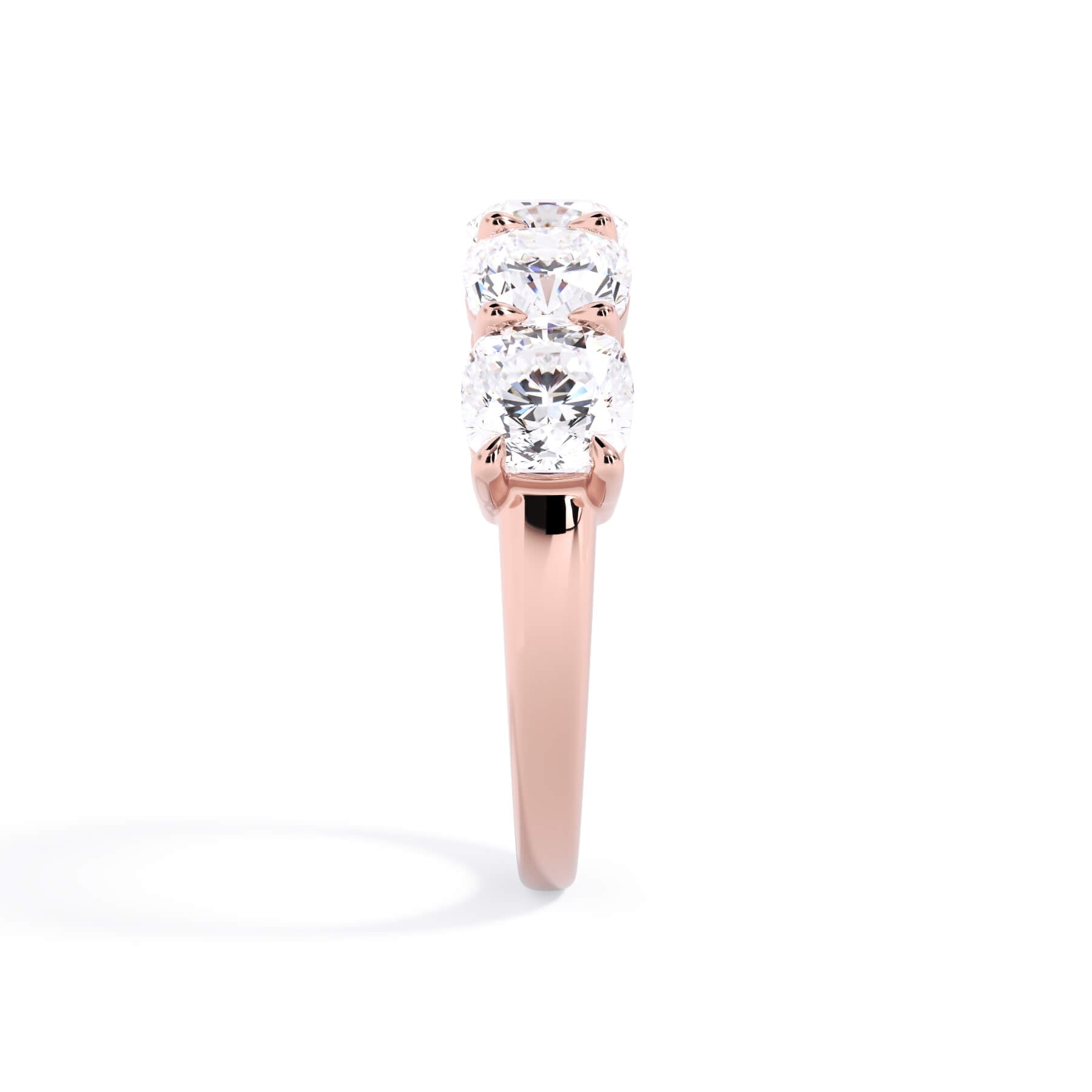 A picture of a five stone diamond wedding ring with cushion shape diamonds that are shared prong set in rose gold on a white background with a side profile view.