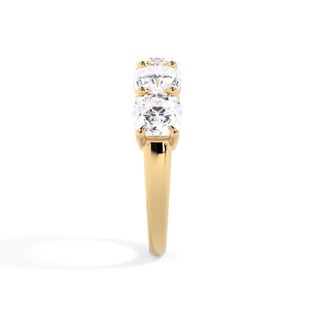 A picture of a five stone diamond wedding ring with cushion shape diamonds that are shared prong set in yellow gold on a white background with a side profile view.
