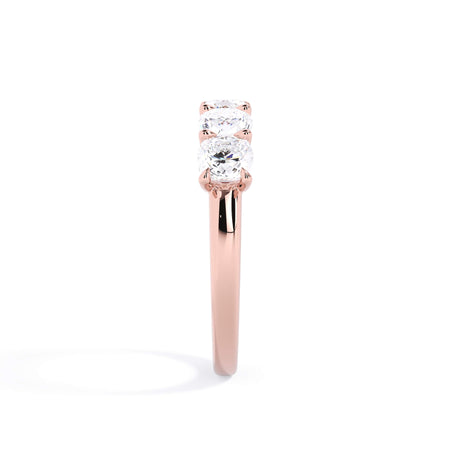 A picture of a five stone diamond wedding ring with cushion shape diamonds that are u prong set in rose gold on a white background with a side profile view.