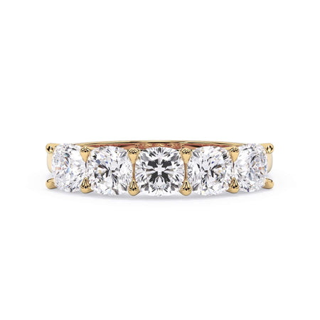 A picture of a five stone diamond wedding ring with cushion shape diamonds that are u prong set in yellow gold on a white background with the ring facing forward, lying down.