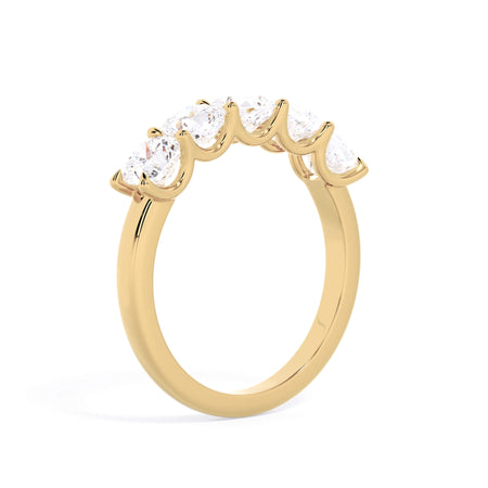 A picture of a five stone diamond wedding ring with cushion shape diamonds that are u prong set in yellow gold on a white background with a slightly angled, through the finger view.