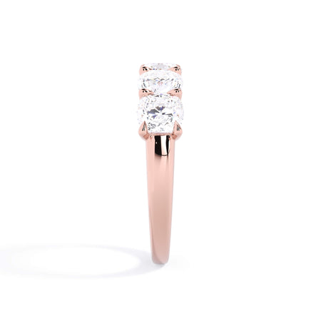 A picture of a five stone diamond wedding ring with cushion shape diamonds that are u prong set in rose gold on a white background with a side profile view.