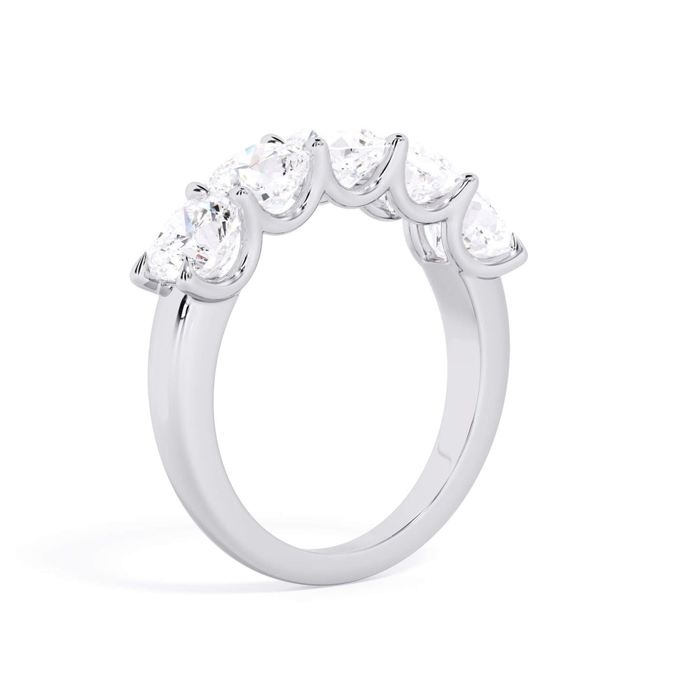 A picture of a five stone diamond wedding ring with cushion shape diamonds that are u prong set in white gold or platinum on a white background with a slightly angled, through the finger view.