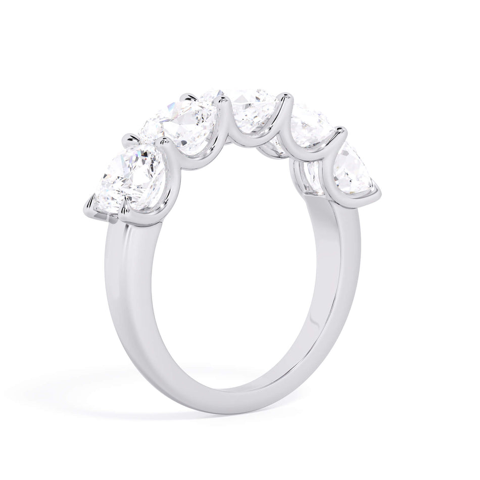 A picture of a five stone diamond wedding ring with cushion shape diamonds that are u prong set in white gold or platinum on a white background with a slightly angled, through the finger view.